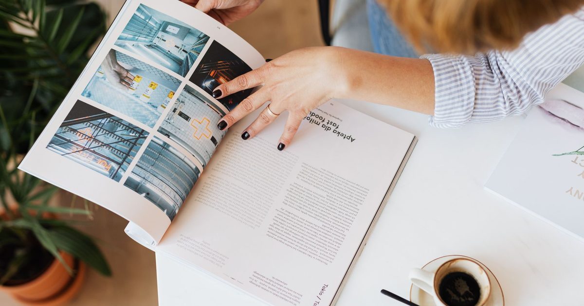 يدان تتصفّحان مجلة على المكتب إلى جانب فنجان قهوة