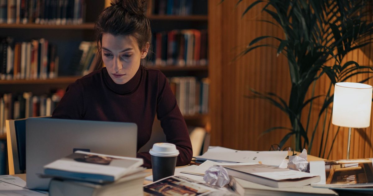 امرأة تعمل إلى مكتب تغطّيه كتب مفتوحة وحاسوب محمول